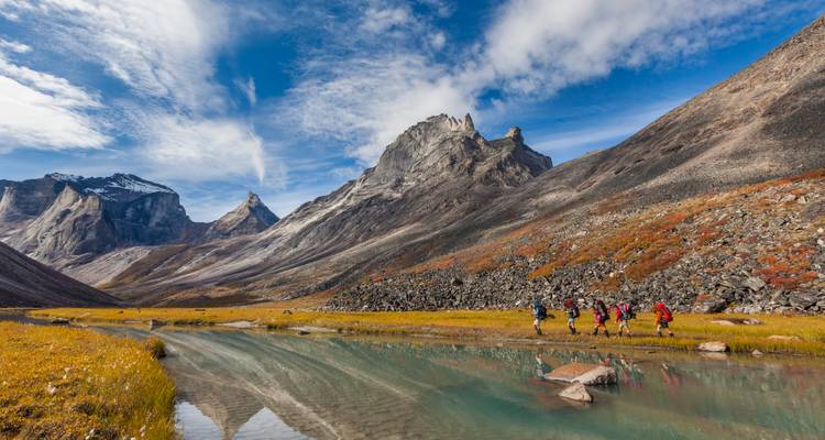 Gruppe von Wanderern, die einen Fluss in einem dramatischen Bergtal überqueren.