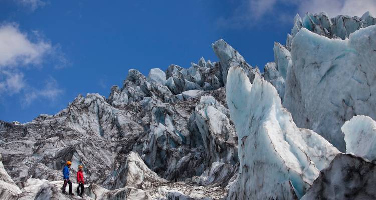 Dos personas caminando en un glaciar con formaciones de hielo dentadas.
