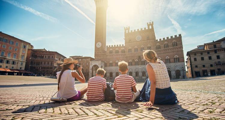 Gezin zittend op een historisch plein genietend van het zonlicht voor een toren.