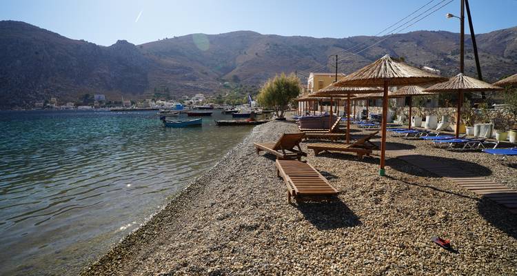 Plage de galets tranquille avec des transats en bois, de petits bateaux et des collines arides en arrière-plan