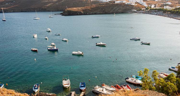 Baie calme parsemée de petits bateaux observée depuis une colline avec des terrasses arides et un village lointain