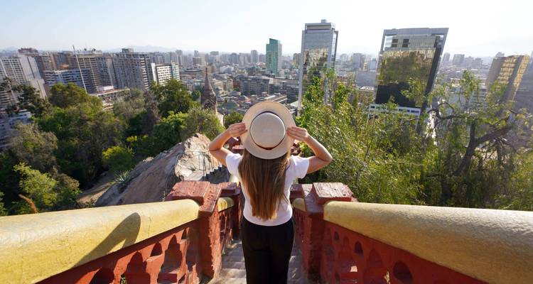 Frau mit Hut betrachtet eine Stadtlandschaft von einer Treppe aus.