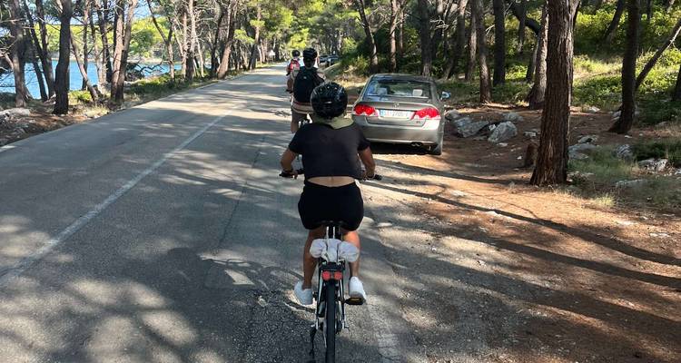 Des personnes à vélo sur une route traversant une zone boisée, avec une voiture garée sur le côté.