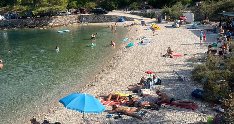Une plage de galets avec des gens qui prennent un bain de soleil et nagent dans une eau claire.