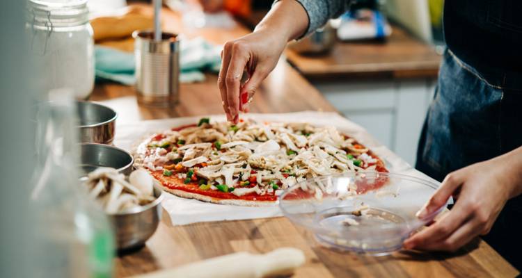 Person preparing a pizza with various toppings.