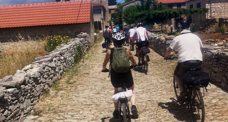 Groupe de personnes faisant du vélo sur un chemin pavé à travers un village rustique.