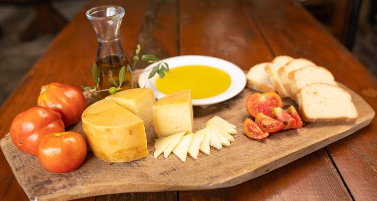 Planche en bois avec fromage, tomates, huile d'olive et pain sur une table.
