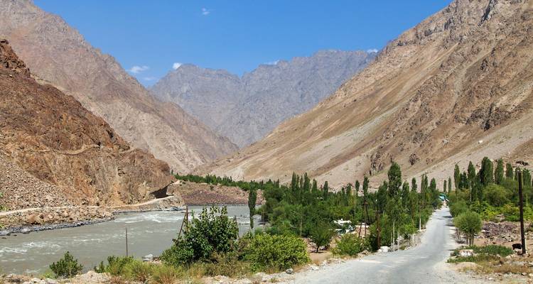 Mountain road alongside a river, surrounded by greenery.