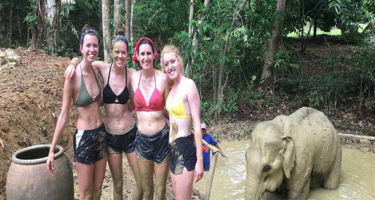 Des femmes qui posent en s'amusant avec un bébé éléphant dans la boue.