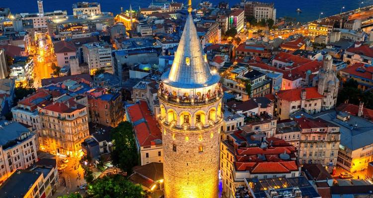 Illuminated Galata Tower rises over Istanbul's vibrant evening skyline and winding streets.