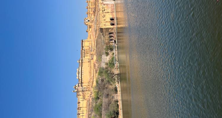 Die goldenen Festungsmauern von Amber Fort erstrecken sich über einen Hügel oberhalb eines ruhigen Sees unter wolkenlosem Himmel.