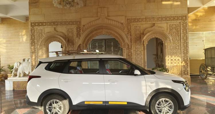 White SUV parked in front of an ornate sandstone palace entrance with carved arches and marble floor reflections.