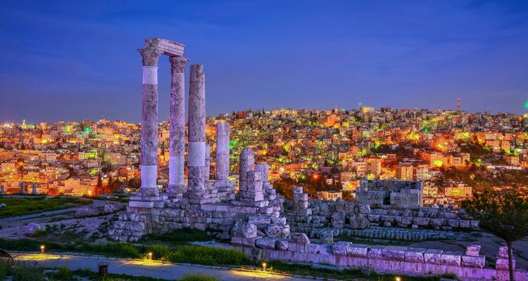 Colonnes romaines d'Amman illuminées la nuit avec vue sur la ville.