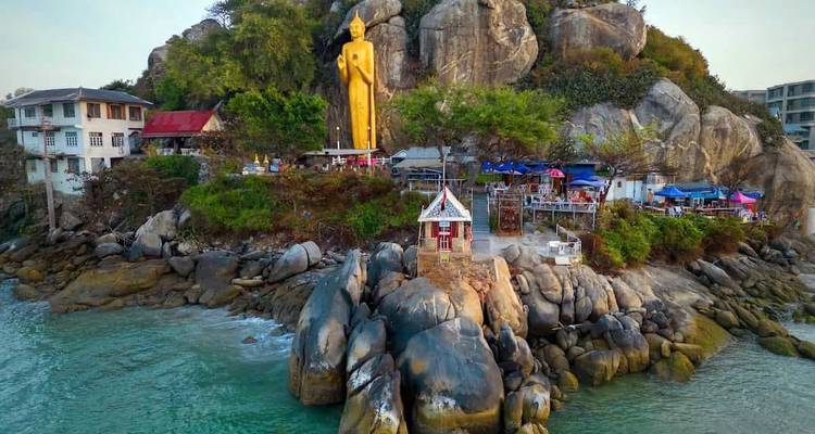Statue dorée de Bouddha sur une colline rocheuse surplombant la mer.