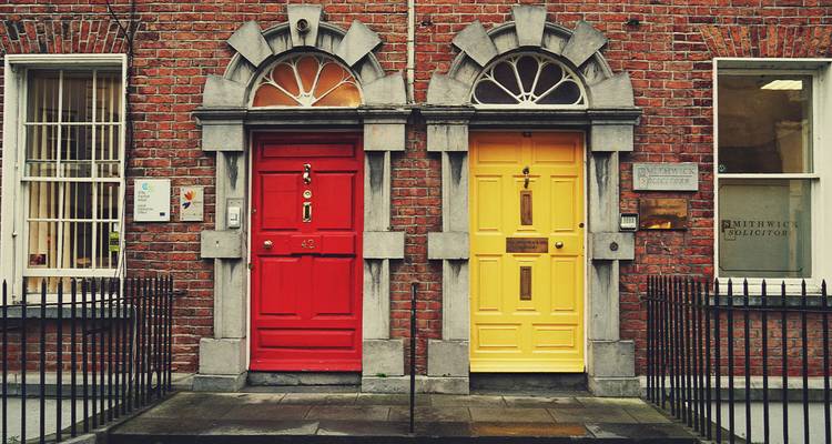 Two brightly painted Georgian doors, one red and one yellow, set in a brick townhouse facade.