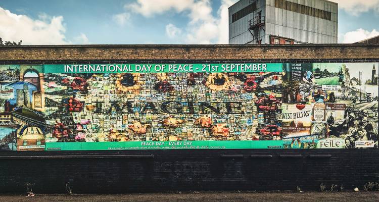 A large colorful mural on a brick peace wall promotes International Day of Peace with the word 'IMAGINE'.