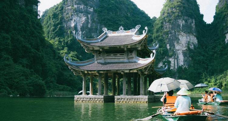 Temple sur l'eau avec des bateaux et des touristes à proximité.