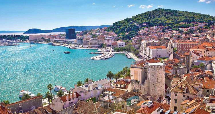 Aerial view of Split’s turquoise harbour, palm-lined promenade and terracotta rooftops backed by forested hills.