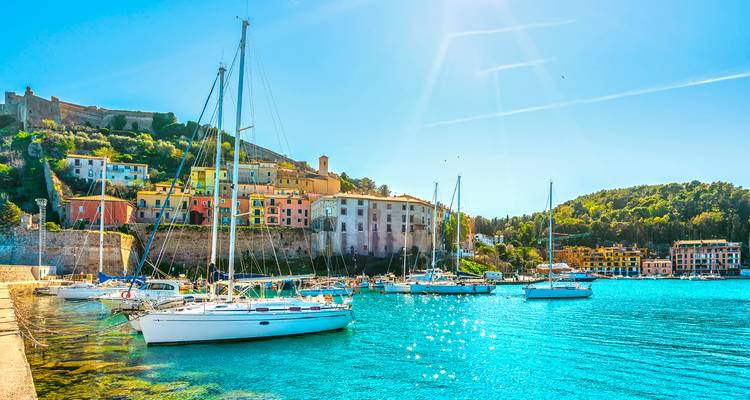 Des bâtiments colorés et des voiliers dans un port côtier par une journée ensoleillée.