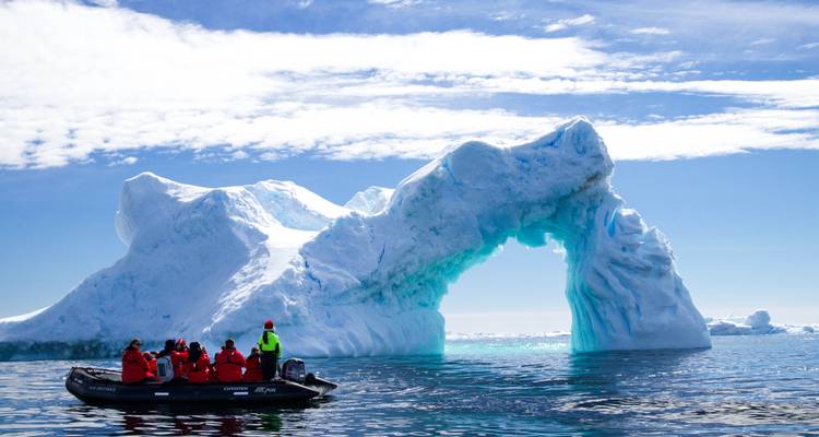 Des gens sur un petit bateau près d'une grande formation de glace avec un ciel bleu.