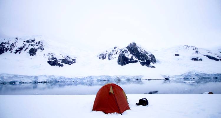 Tente installée dans un paysage glacé avec des montagnes en arrière-plan.