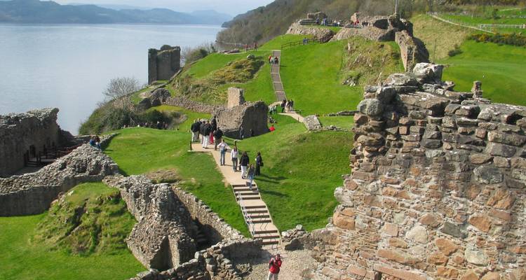Ruines du château d'Urquhart surplombant les eaux paisibles du Loch Ness avec des visiteurs explorant les terres.