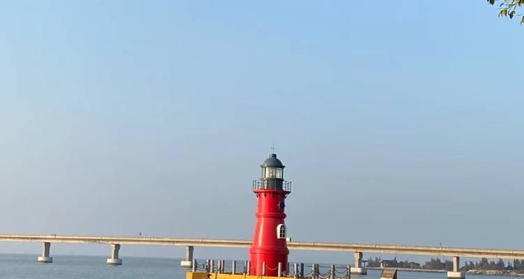 Una vista panorámica de un faro rojo junto al mar y un puente al fondo.