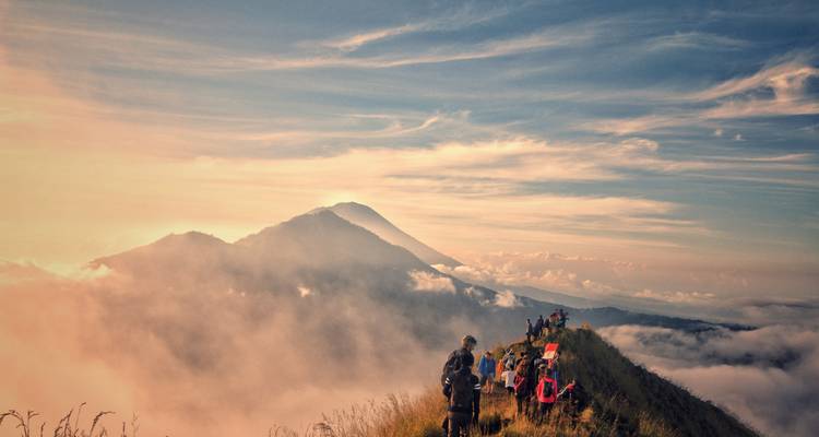 Grupo de excursionistas caminando por una cresta sobre las nubes al amanecer.