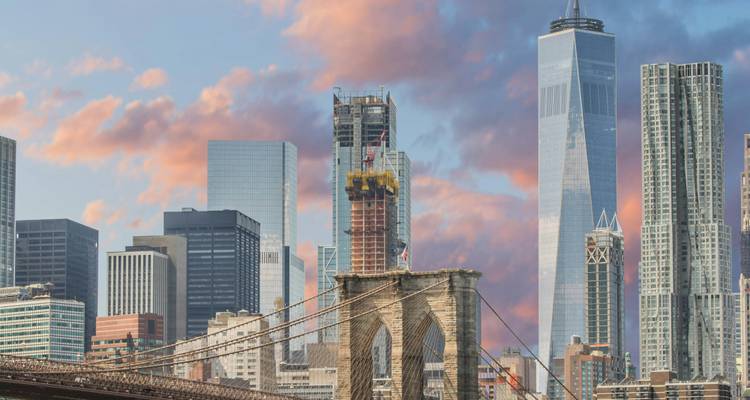 Die Brooklyn Bridge überquert den East River mit dem One World Trade Center und der Skyline von Lower Manhattan bei Sonnenaufgang.