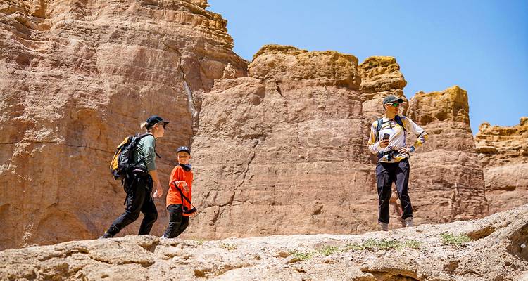 Three people walking along rocky formations in a canyon.