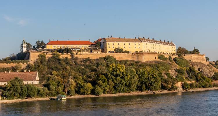 Une longue forteresse perchée sur une colline aux murs jaunes surplombe le Danube à la lumière du coucher de soleil.