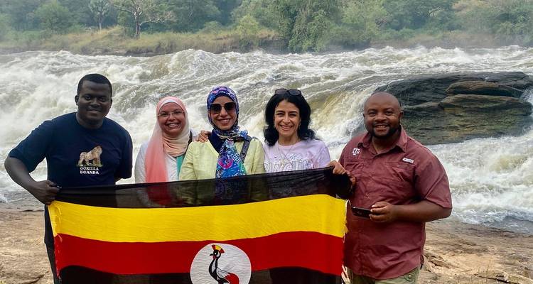 Groupe de personnes tenant un drapeau ougandais devant une cascade.