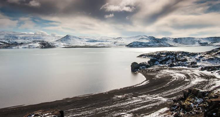 Paisaje montañoso nevado con un lago y playa de arena negra