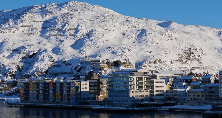 Des immeubles d'appartements colorés à la base d'une montagne enneigée à côté d'un fjord arctique.