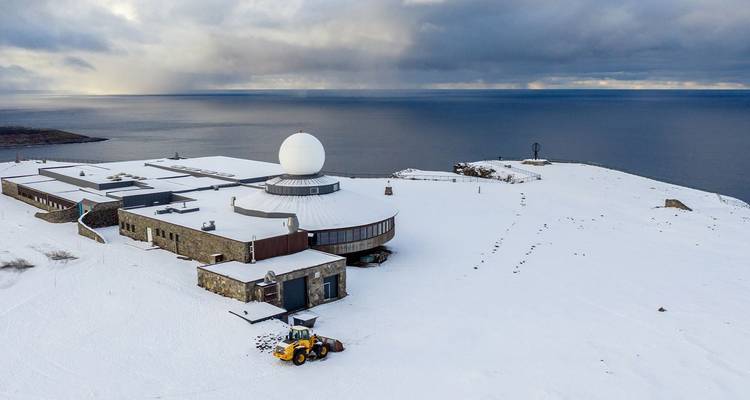 Station radar côtière arctique isolée dotée d'un grand dôme blanc situé sur un promontoire enneigé dominant la mer.