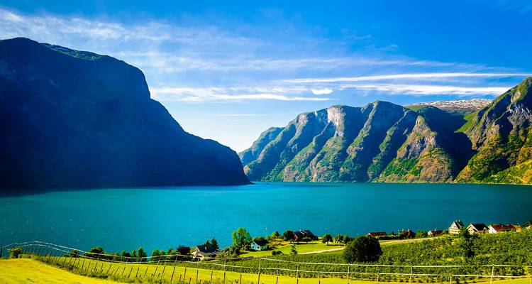 Un fiordo azul brillante rodeado de montañas verdes escarpadas y un pequeño pueblo junto al lago en Noruega.