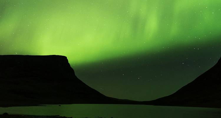 Aurora boreal verde barriendo un cielo oscuro sobre un tranquilo valle ártico y un lago.