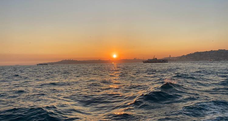Sunset over the sea with boats on the horizon.