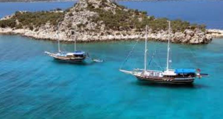 Zeilboten op turquoise water bij een rotsachtig eiland.