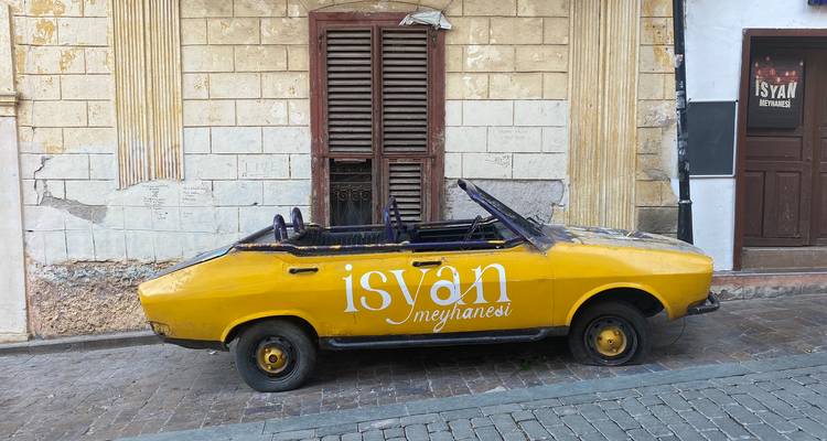 Gele cabriolet geparkeerd tegen een oude gebouwmuur.