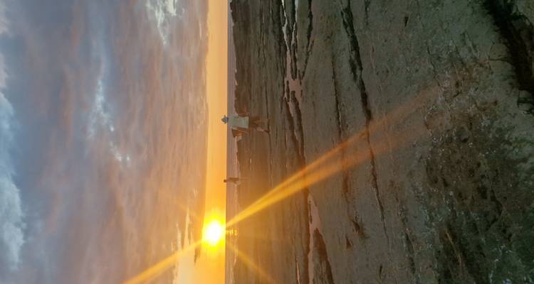 Personne marchant le long d'un littoral rocheux pendant un coucher de soleil éclatant.