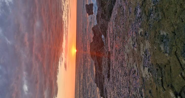Soleil se couchant sur l'océan avec un premier plan rocheux.