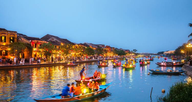 Night view of lantern boats on the river with bustling activity and illuminated buildings.