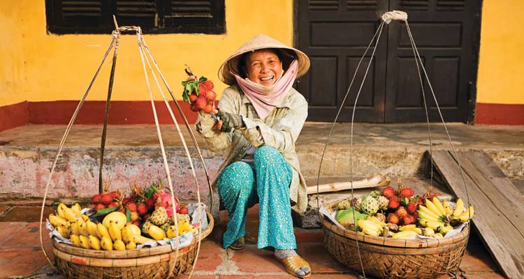 Smiling vendor with baskets of fruit.