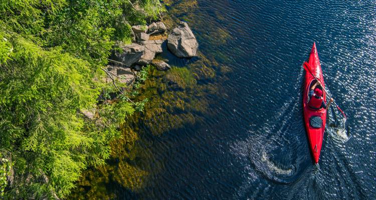 Une vue aérienne d'un kayakiste dans un kayak rouge pagayant sur une rivière entourée de verdure.