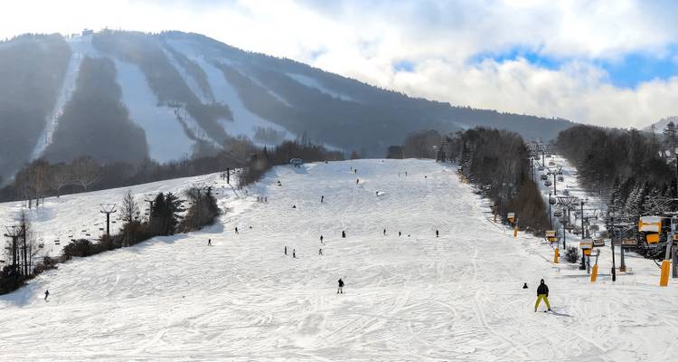 Skieurs sur une pente enneigée avec des remontées mécaniques en arrière-plan.