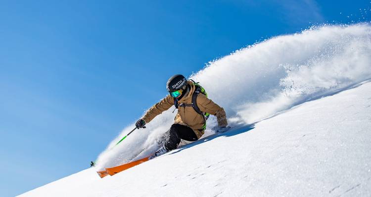 Un skieur effectuant un virage sur une pente enneigée avec une gerbe de neige.