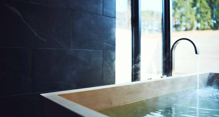 Baignoire fumante près d'une fenêtre dans une pièce sombre en pierre.