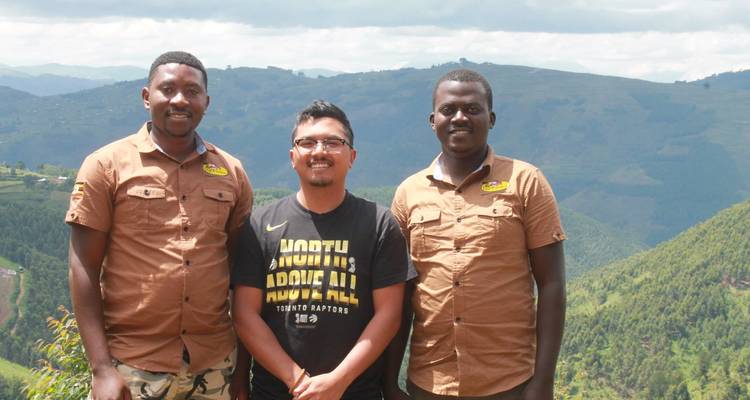 Three men posing in front of lush green hills