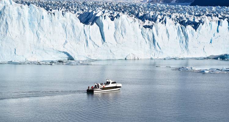 Boat cruising near the edge of a massive glacier wall.
